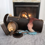 Leather knitting bag and spinning accessories with multicolored wool fiber in front of a fireplace.