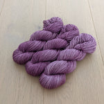 Purple yarn skeins on a light wooden floor, ready for knitting or crocheting projects.