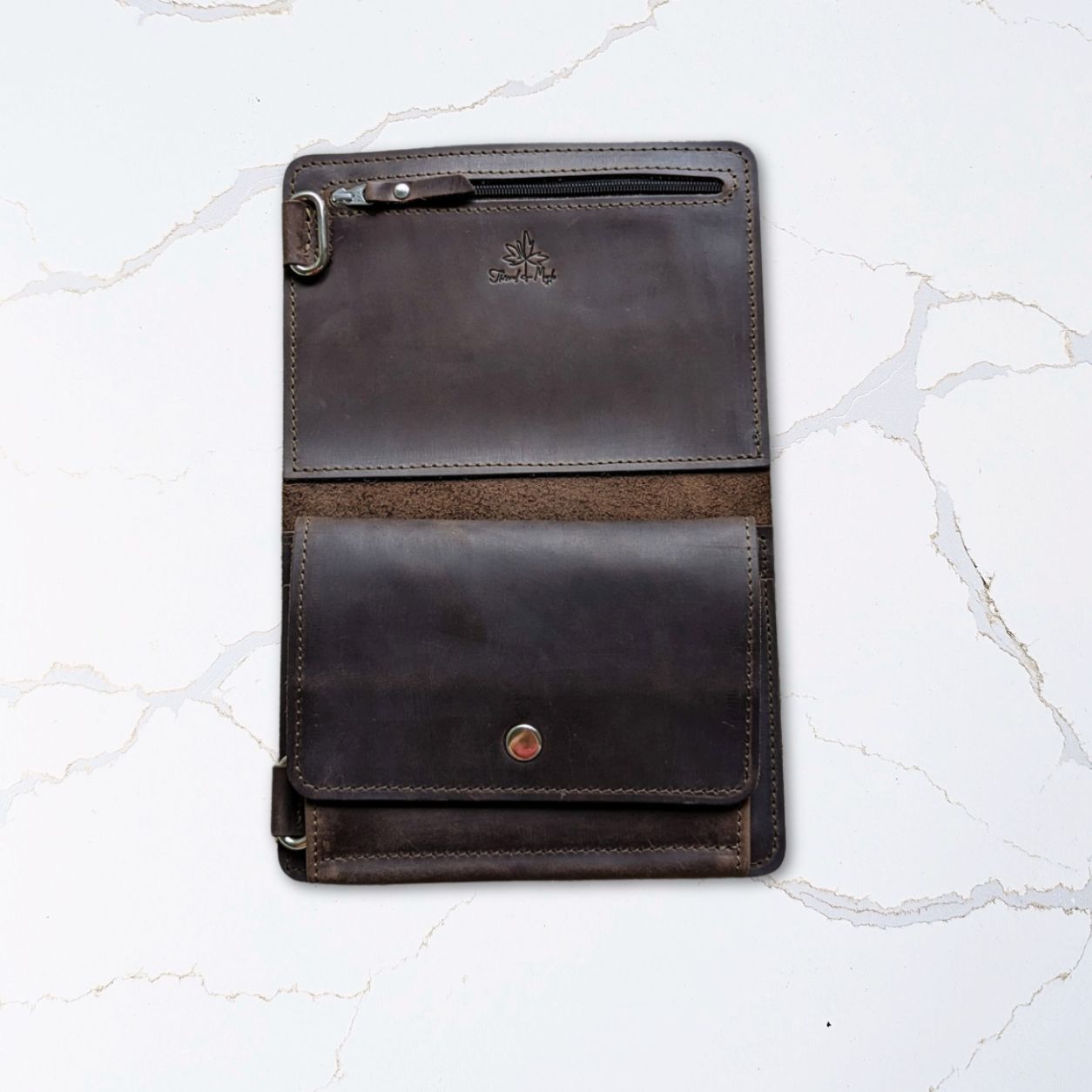 Dark leather tablet case with a button closure and slot for stylus, placed on a white marble surface.