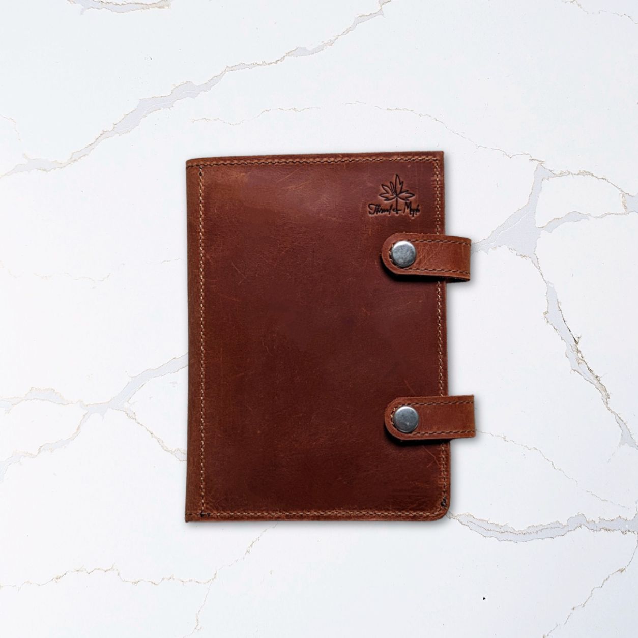 Brown leather notebook with metal button closures on white marble surface.