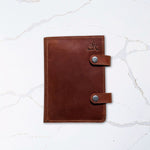 Brown leather journal with button clasps on a white marble surface