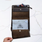 Open brown leather wallet on marble surface, showcasing interior compartments holding cards and papers, with a hand holding the wallet.
