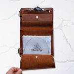 Brown leather travel wallet with pen and document pocket on white marble background.