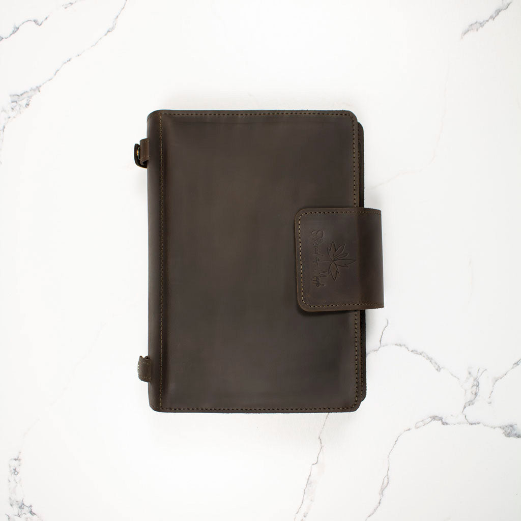 Dark leather notebook cover with snap closure on a white marble background.