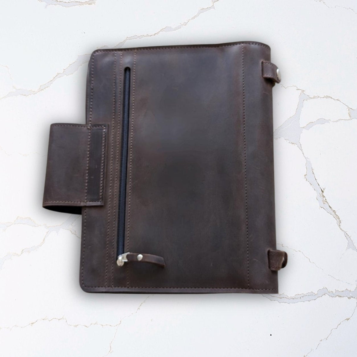 Brown leather portfolio notebook cover on a white marble background.
