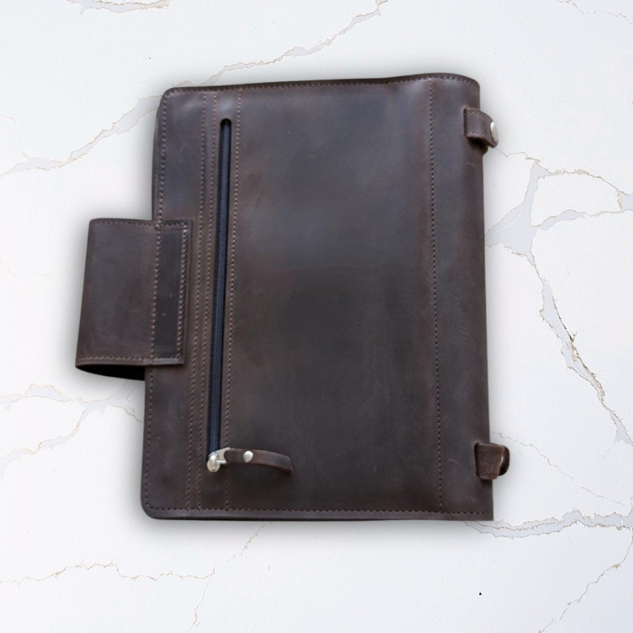 Brown leather portfolio notebook cover on a white marble background.