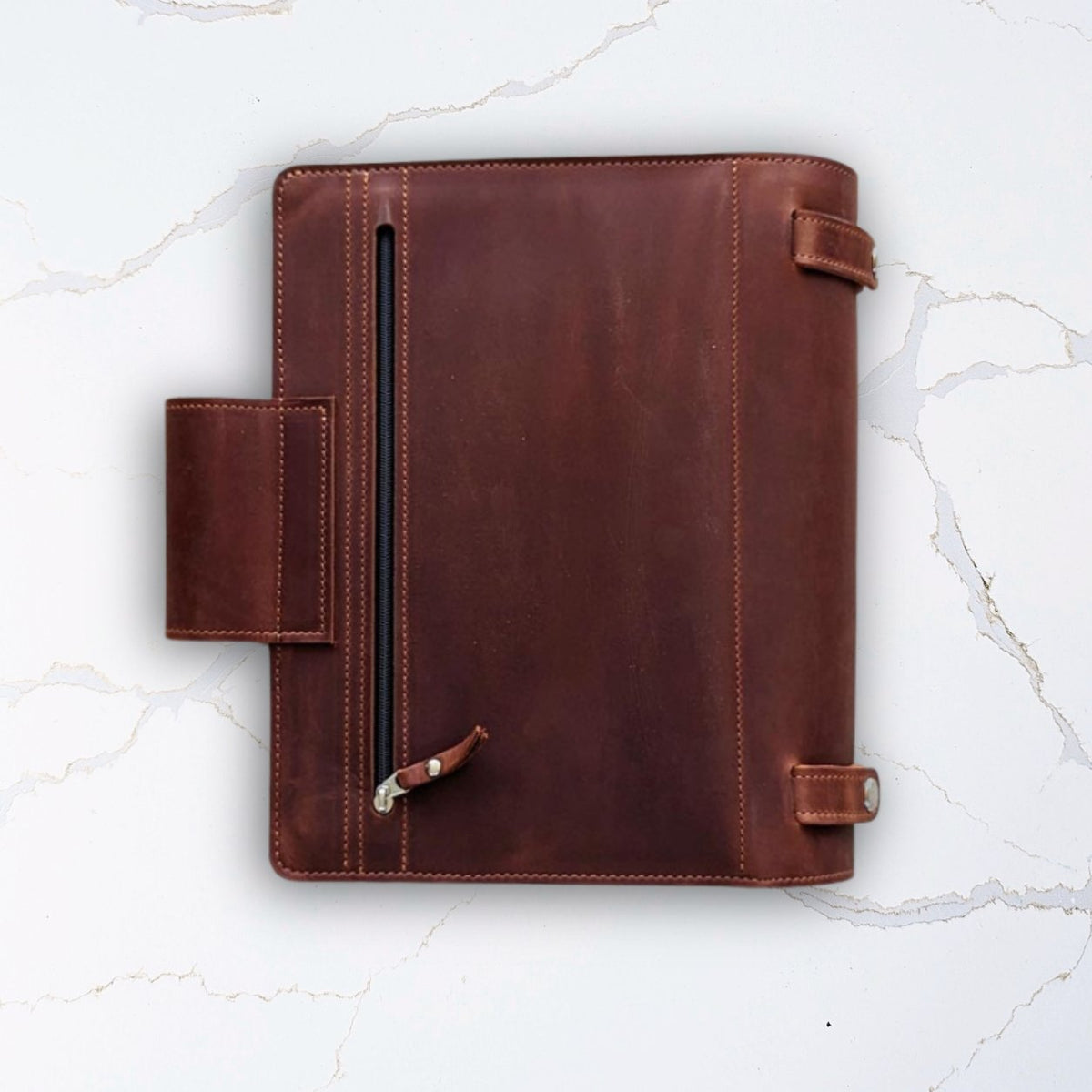 Brown leather portfolio folder with zipper pocket on white marble background