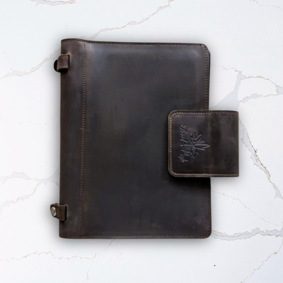Dark brown leather journal with clasp on a marble surface.