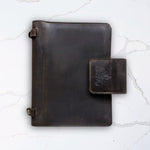 Dark brown leather journal with clasp on a marble surface.