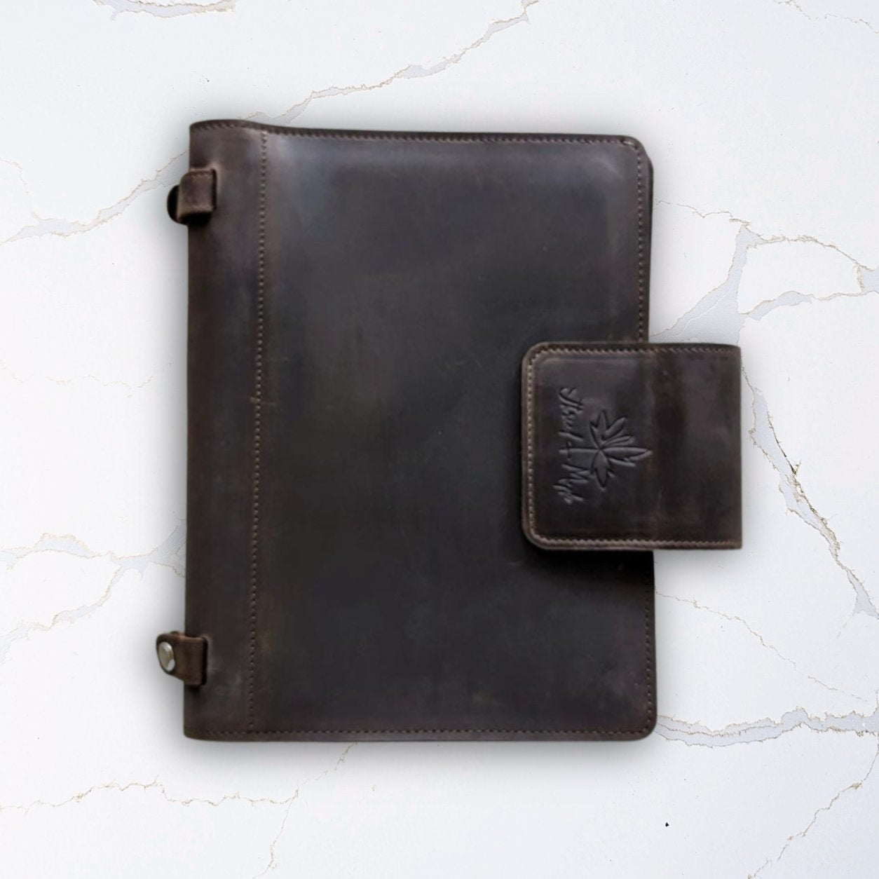 Dark brown leather journal with clasp on a marble surface.