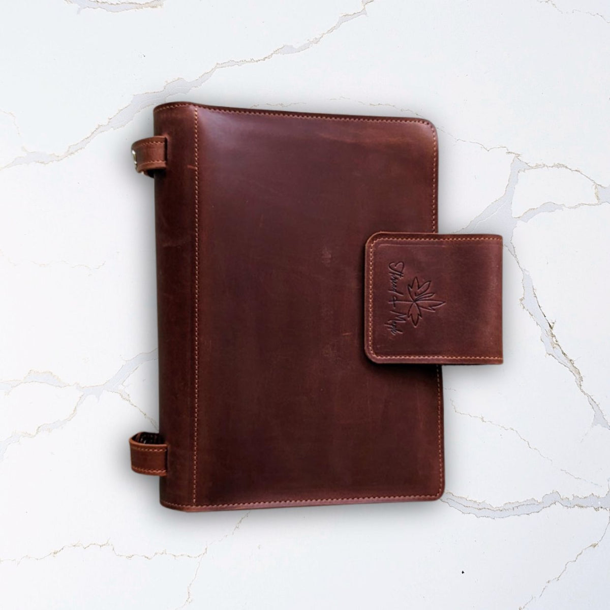 Brown leather notebook with a clasp on a white marble background.