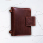 Brown leather notebook with a clasp on a white marble background.