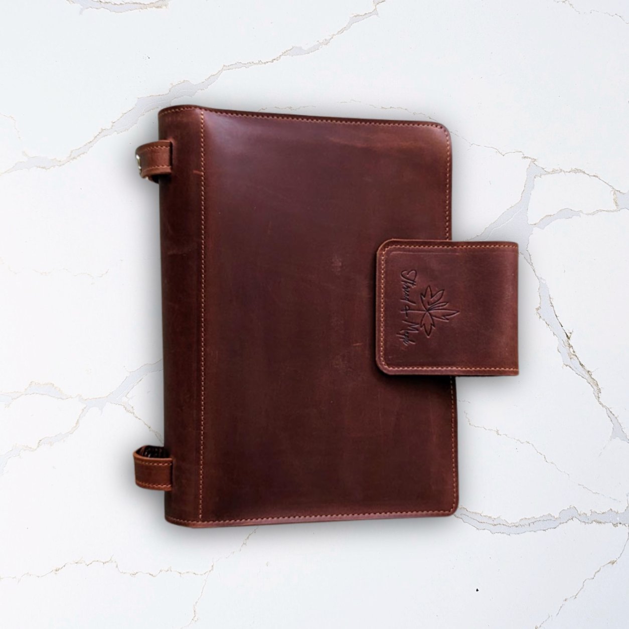 Brown leather notebook with a clasp on a white marble background.