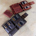 Leather notebook and pen holders laid out on a beige surface with various compartments featuring different colors and sizes.