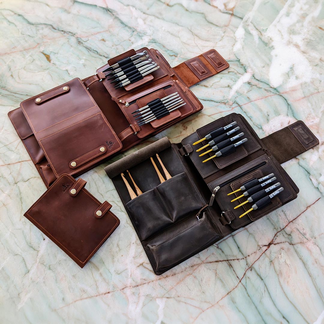 Leather tool cases with various artist brushes and tools displayed on a marble surface.