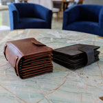 Two leather wallets, one brown and one black, placed on a marble table with blue chairs in the background.