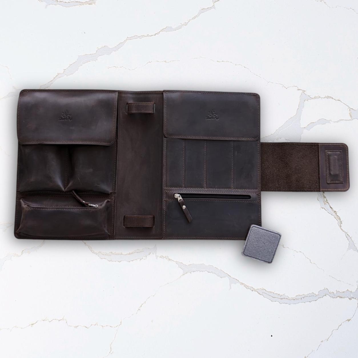 Dark brown leather travel organizer with multiple compartments, including a pen slot, on a light marble surface.