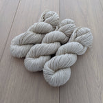 Four skeins of light beige yarn arranged on a wooden surface.