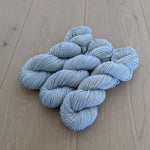 Light gray yarn skeins arranged on a wooden floor.