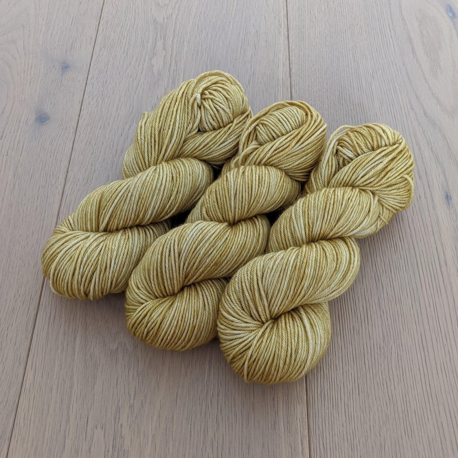 Three skeins of yellow yarn on a wooden surface.