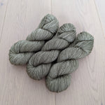 Four skeins of green yarn neatly arranged on a light wooden surface.
