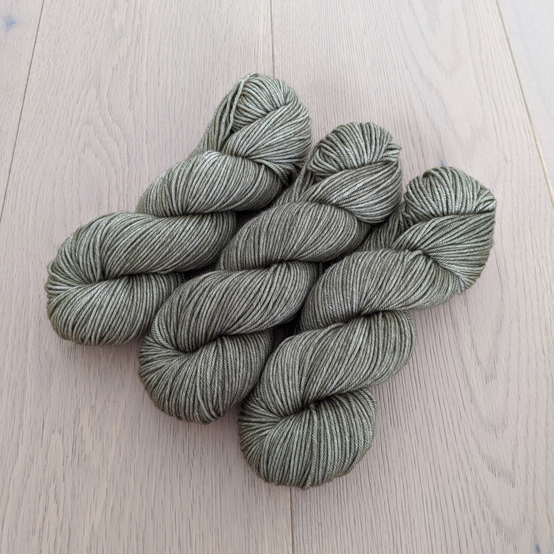 Four skeins of green yarn neatly arranged on a light wooden surface.