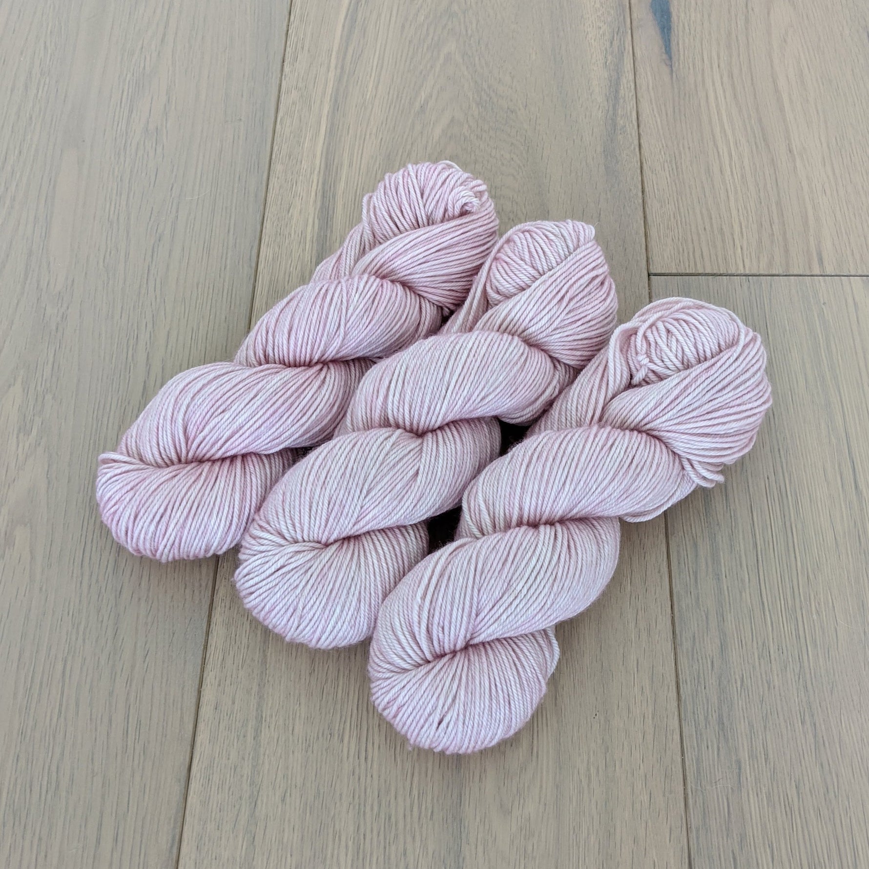 Three skeins of light pink yarn arranged on a wooden floor