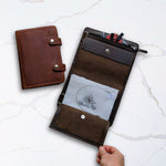 Brown leather wallet and organizer on a marble surface, showcasing multiple pockets and a hand holding the open organizer.