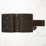 Open brown leather wallet with multiple compartments on a white marble surface.