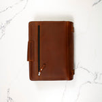 Brown leather binder with a zipper pocket on a marble surface.