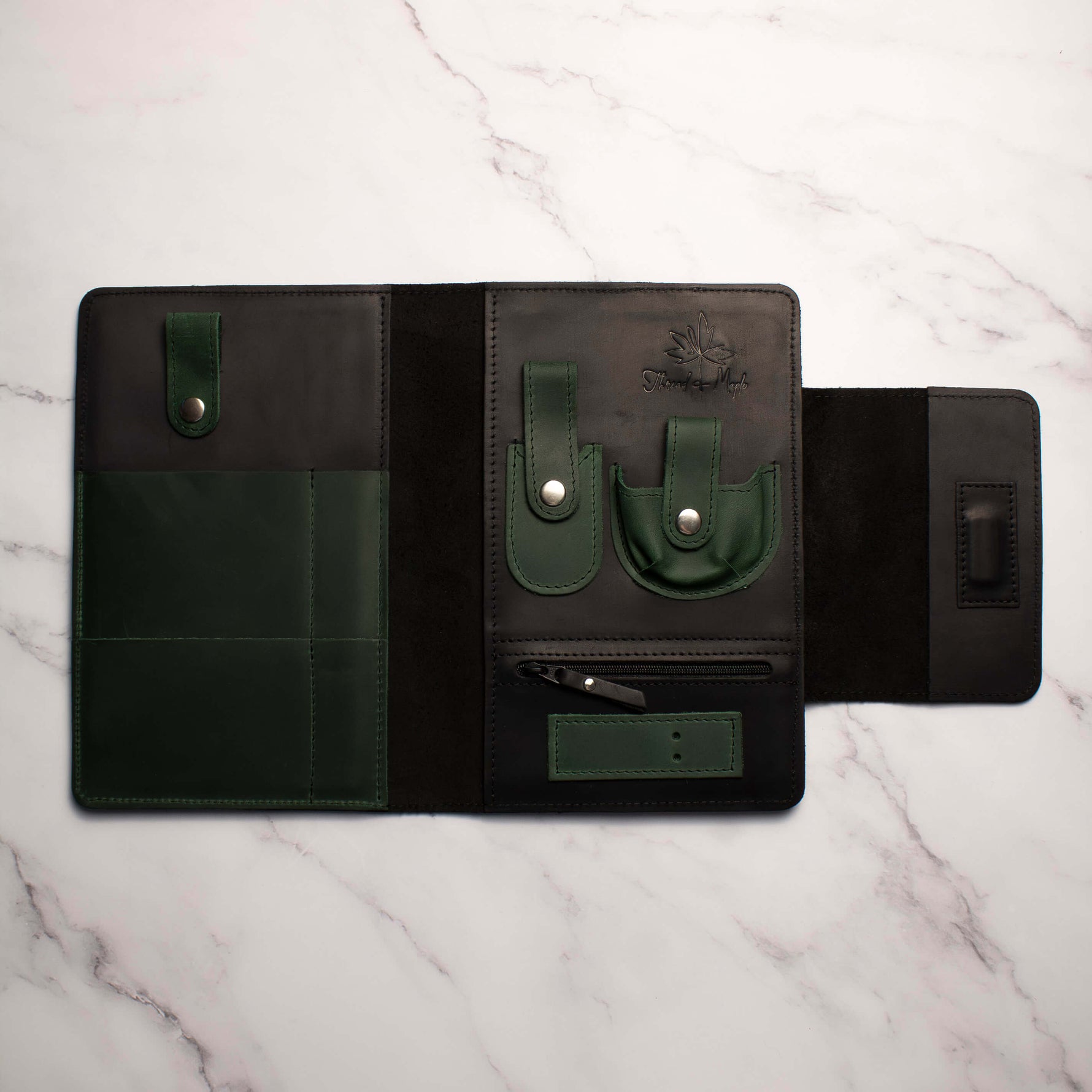 Open black and green leather tool organizer on white marble surface with pockets and snap closures.