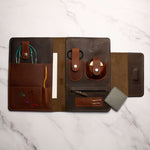 Leather desk organizer with compartments for stationery, cables, and accessories on a marble surface.