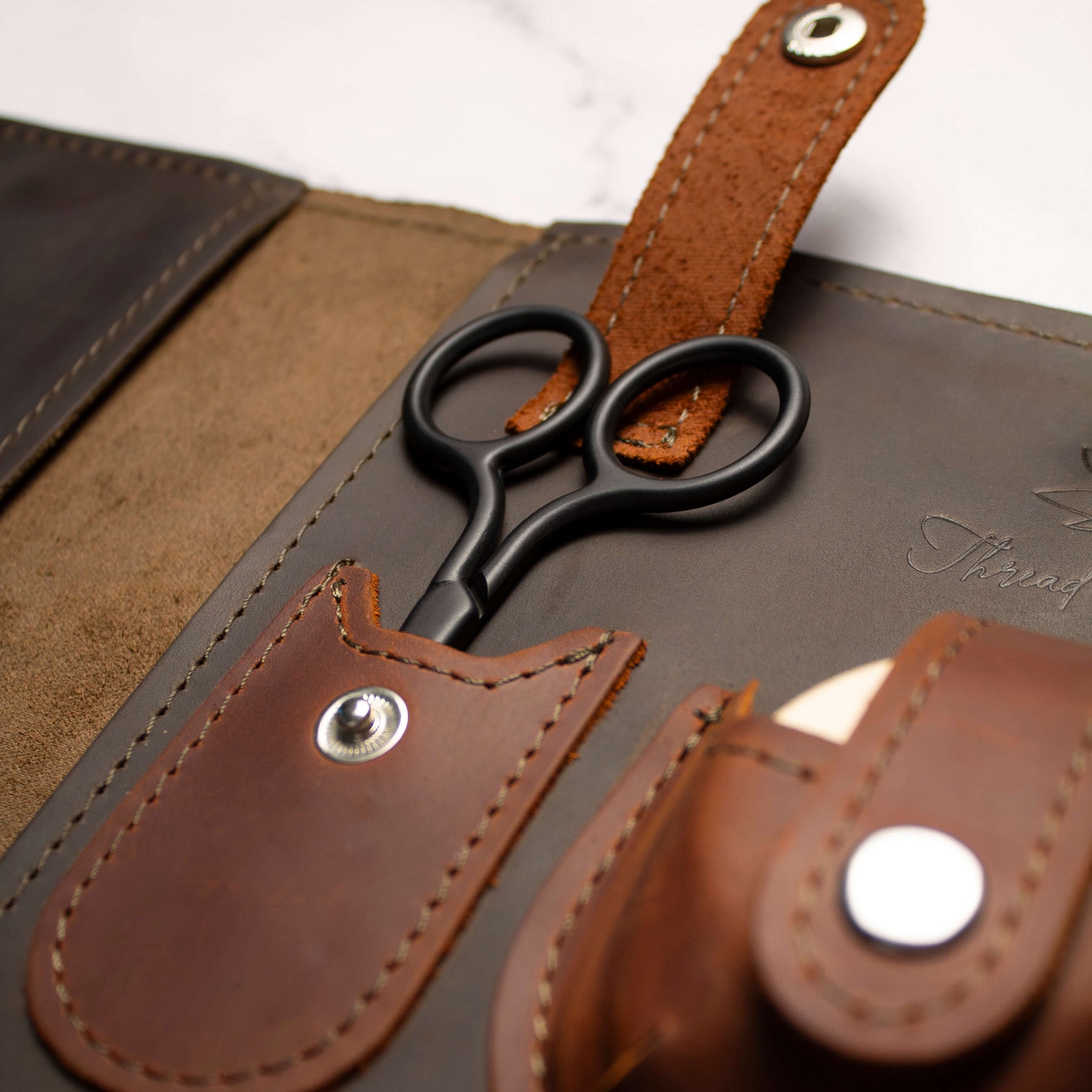Leather case with black scissors in a stylish organizer set on a wooden surface.