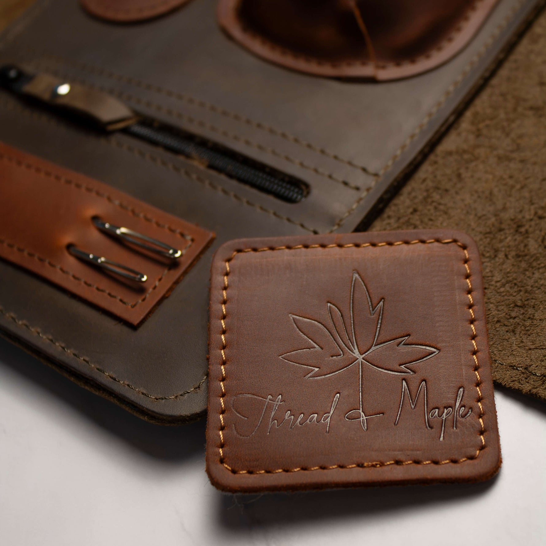 Brown leather wallet with embossed leaf design and pen holder on table surface.