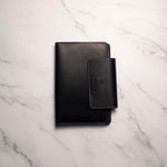 Black leather notebook with pen holder on white marble surface.