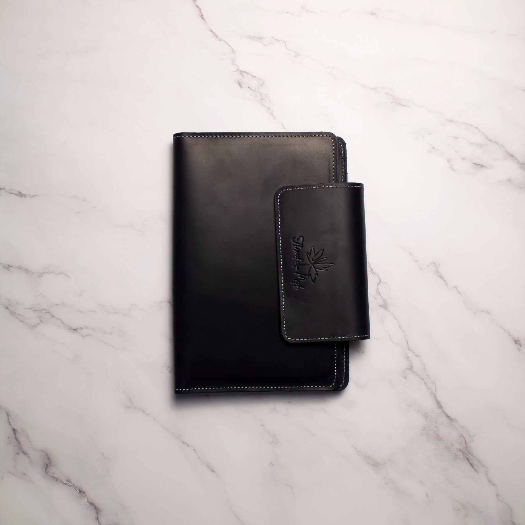 Black leather notebook with pen holder on white marble surface.
