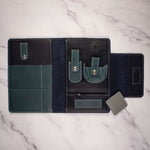 Open leather travel organizer with pockets and straps for tech accessories on a marble surface.