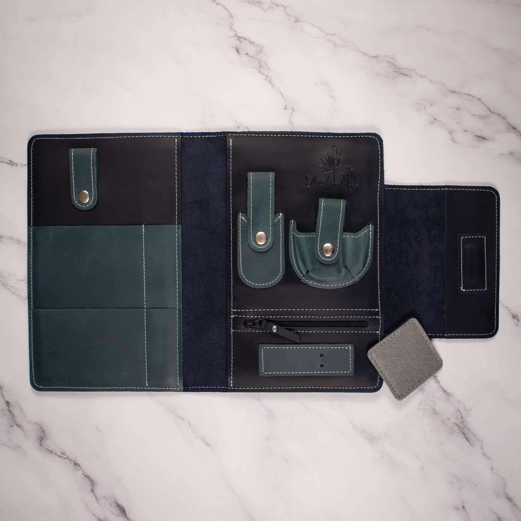 Open leather travel organizer with pockets and straps for tech accessories on a marble surface.