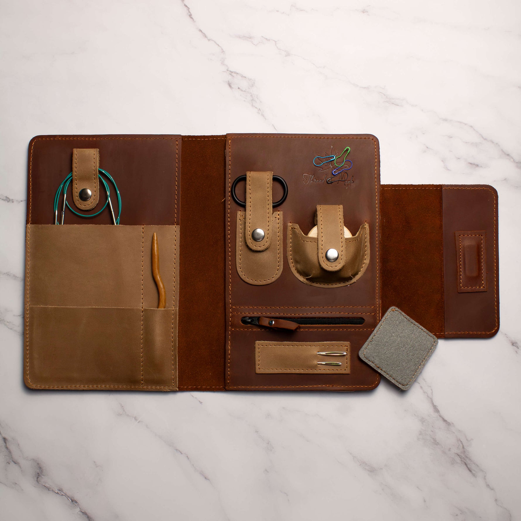 leather tech organizer with multiple compartments holding cables, a pen, and small accessories placed on a marble background