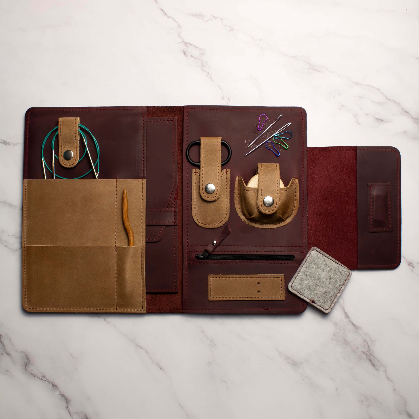 Handcrafted leather knitting needle organizer with multiple compartments on marble background.