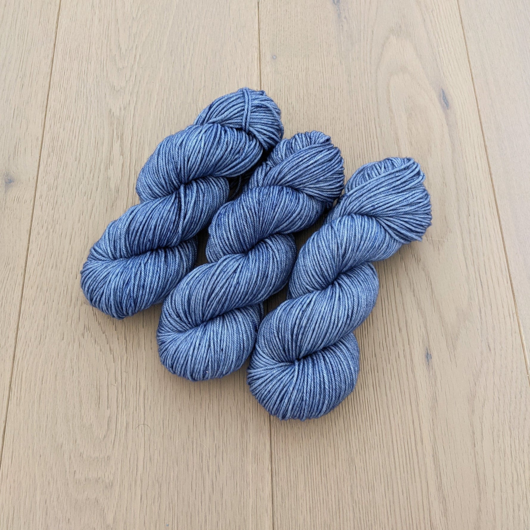 Four skeins of soft blue yarn on a light wooden floor.